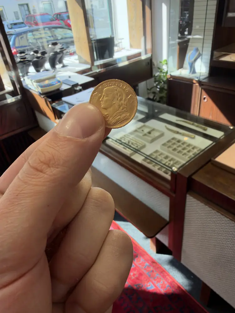 Hand hält ein Schweizer Goldvreneli vor einer Ladentheke mit Schmuckvitrinen