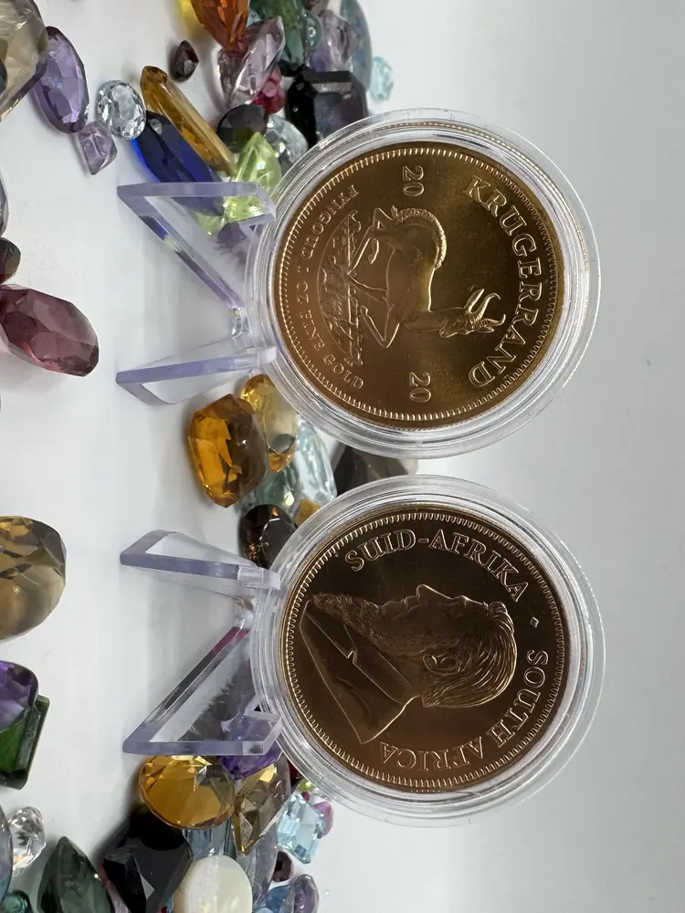 Zwei Krügerrand-Goldmünzen in Münzkapseln zwischen bunten Edelsteinen, Münzhändler in Bremen