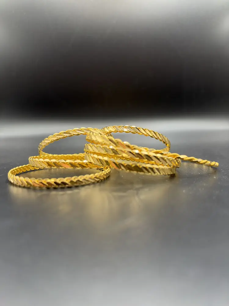 Mehrere goldene Armreifen mit gedrehtem Muster auf dunklem Untergrund
