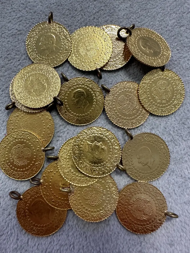 Viele goldfarbene Münzen mit angelöteter Öse auf einem hellen Tuch