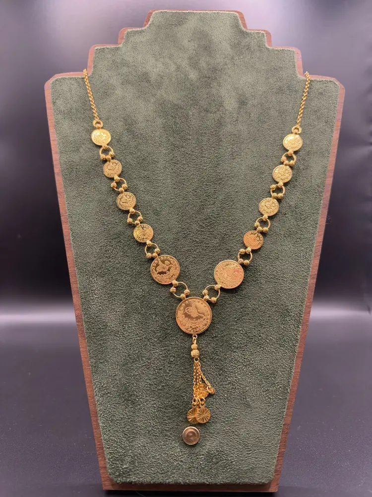 Goldfarbene Münzkette mit Anhänger auf grünem Samtdisplay